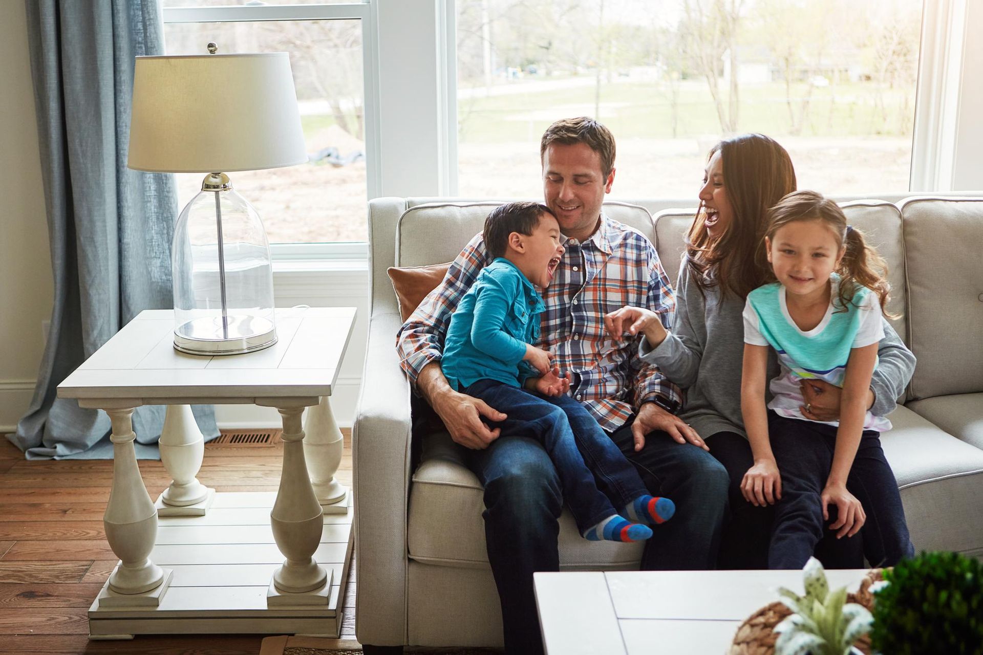 Family sitting on a couch in a bright living room, with a child on each side of an adult man.