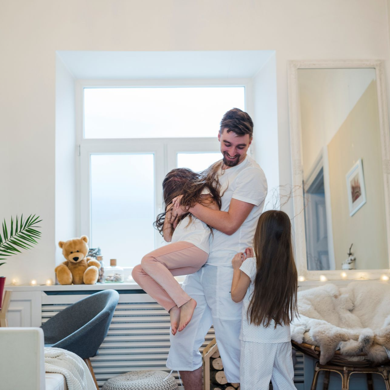 Family embracing in a bright living room, with a father holding a child and a girl standing nearby
