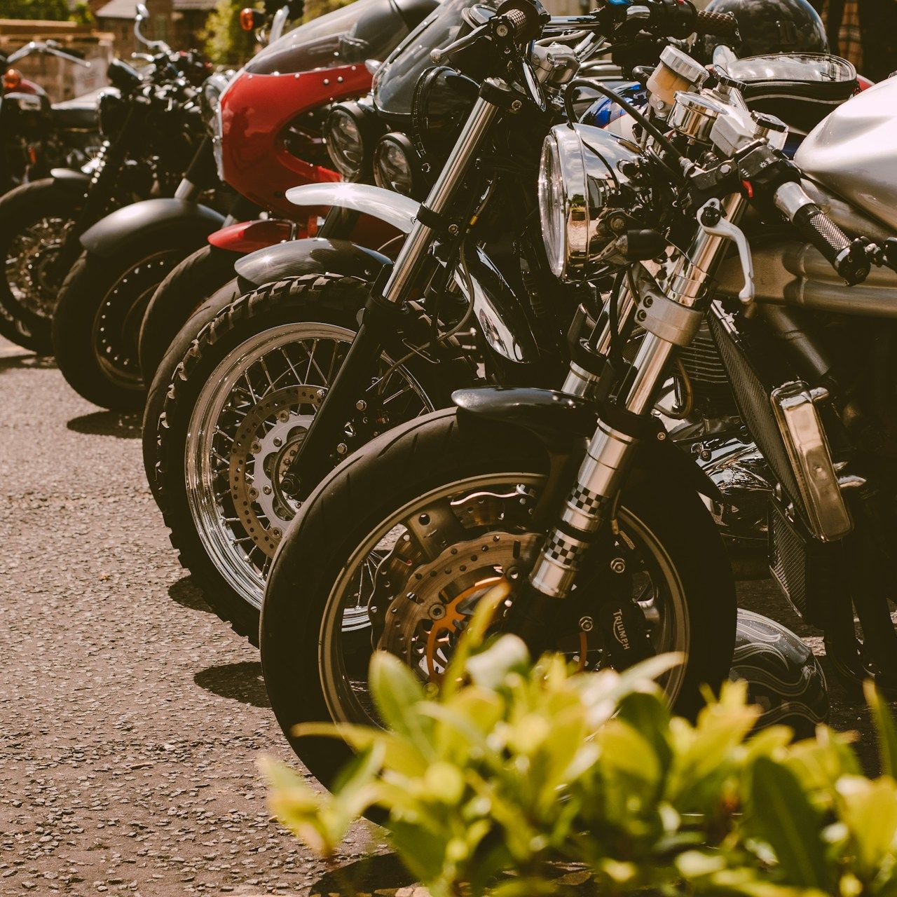 Parked motorcycles lined up outdoors, with a red bike and chrome details in the foreground.