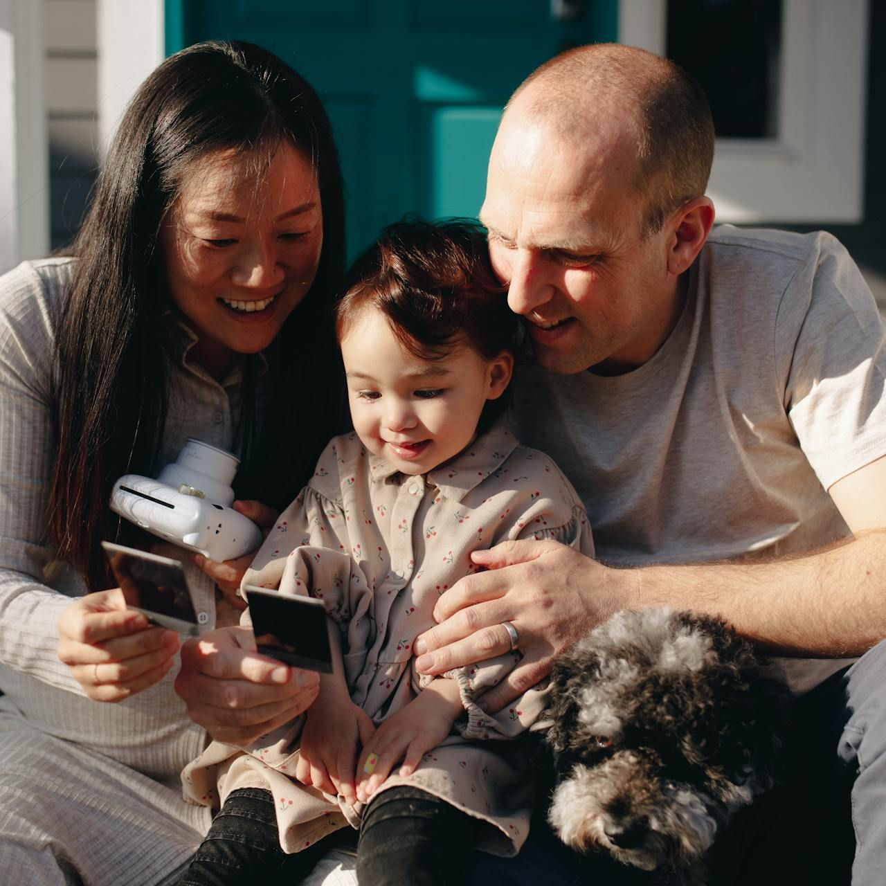 Family gathered on a couch, smiling while looking at a book with a small dog beside them.