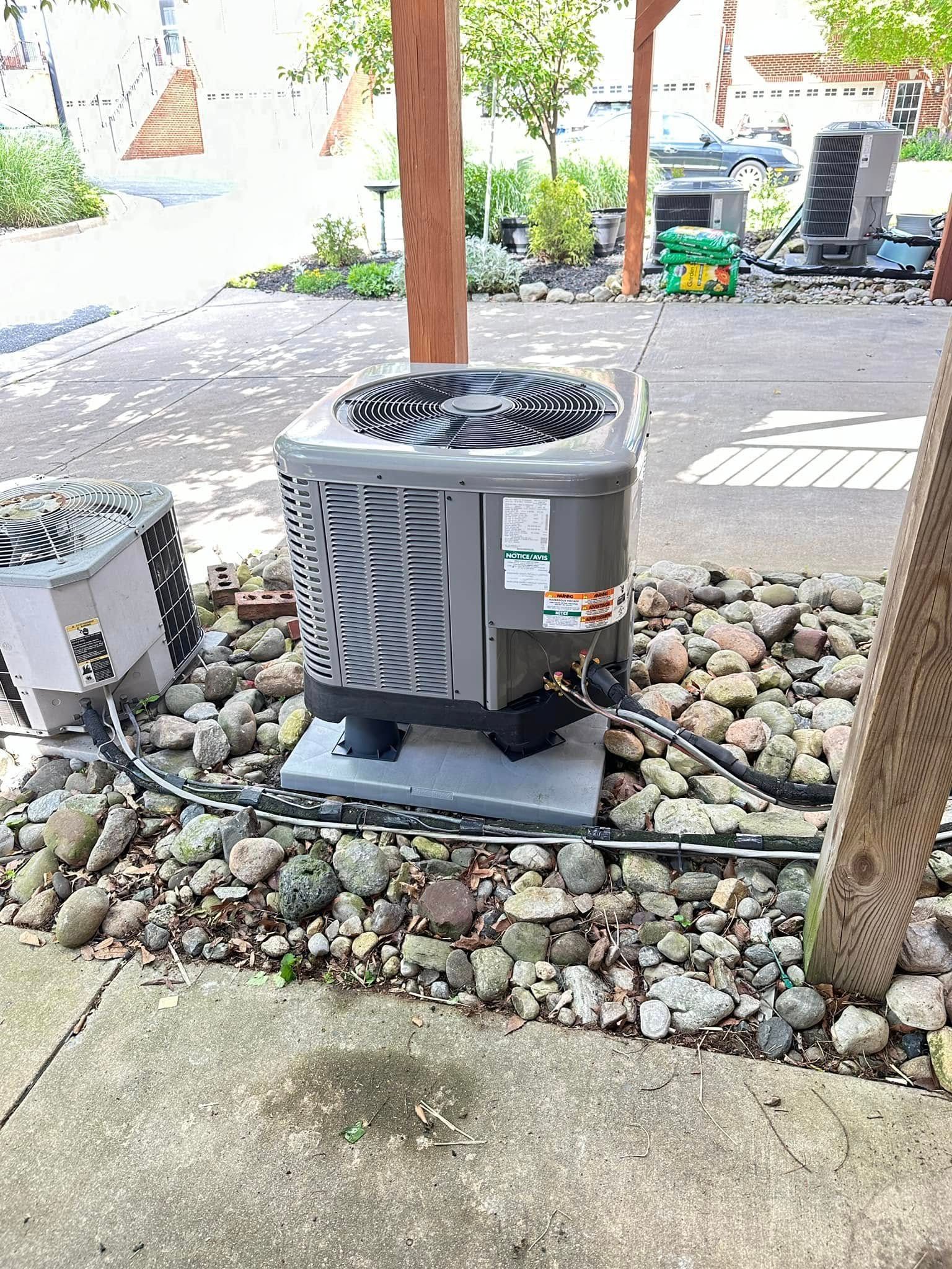 Outdoor air conditioning unit on a gravel pad beside a patio and wooden posts.