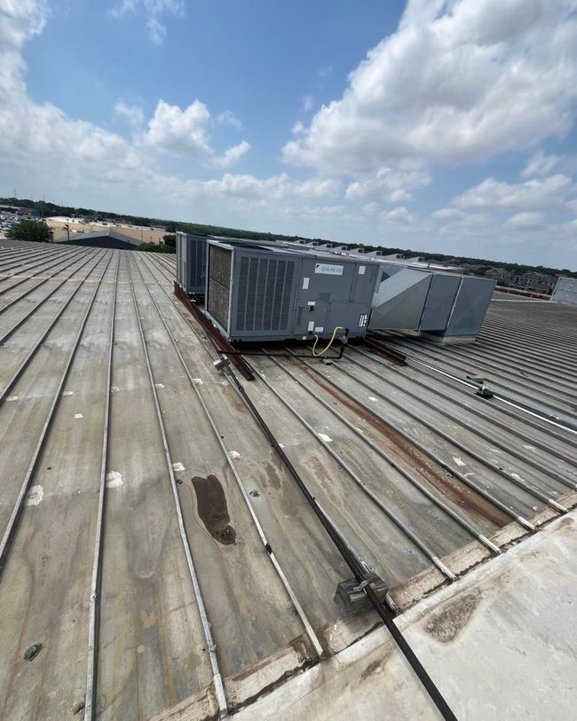 Rooftop HVAC units on a weathered metal roof under a partly cloudy sky.