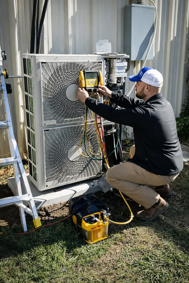 Technician testing an outdoor HVAC unit beside a house with a multimeter and tools