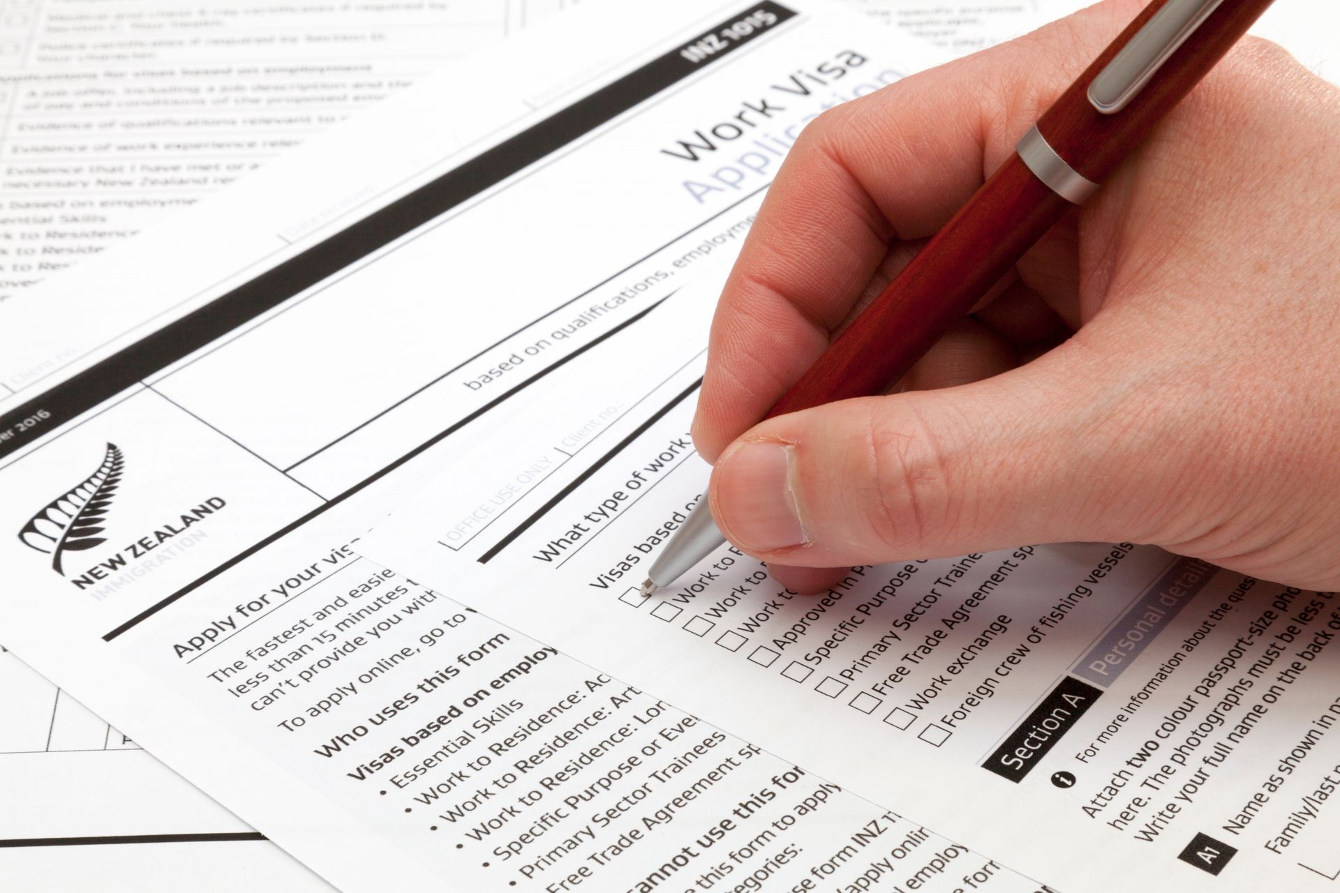 Hand holding a pen filling out a New Zealand work visa application.