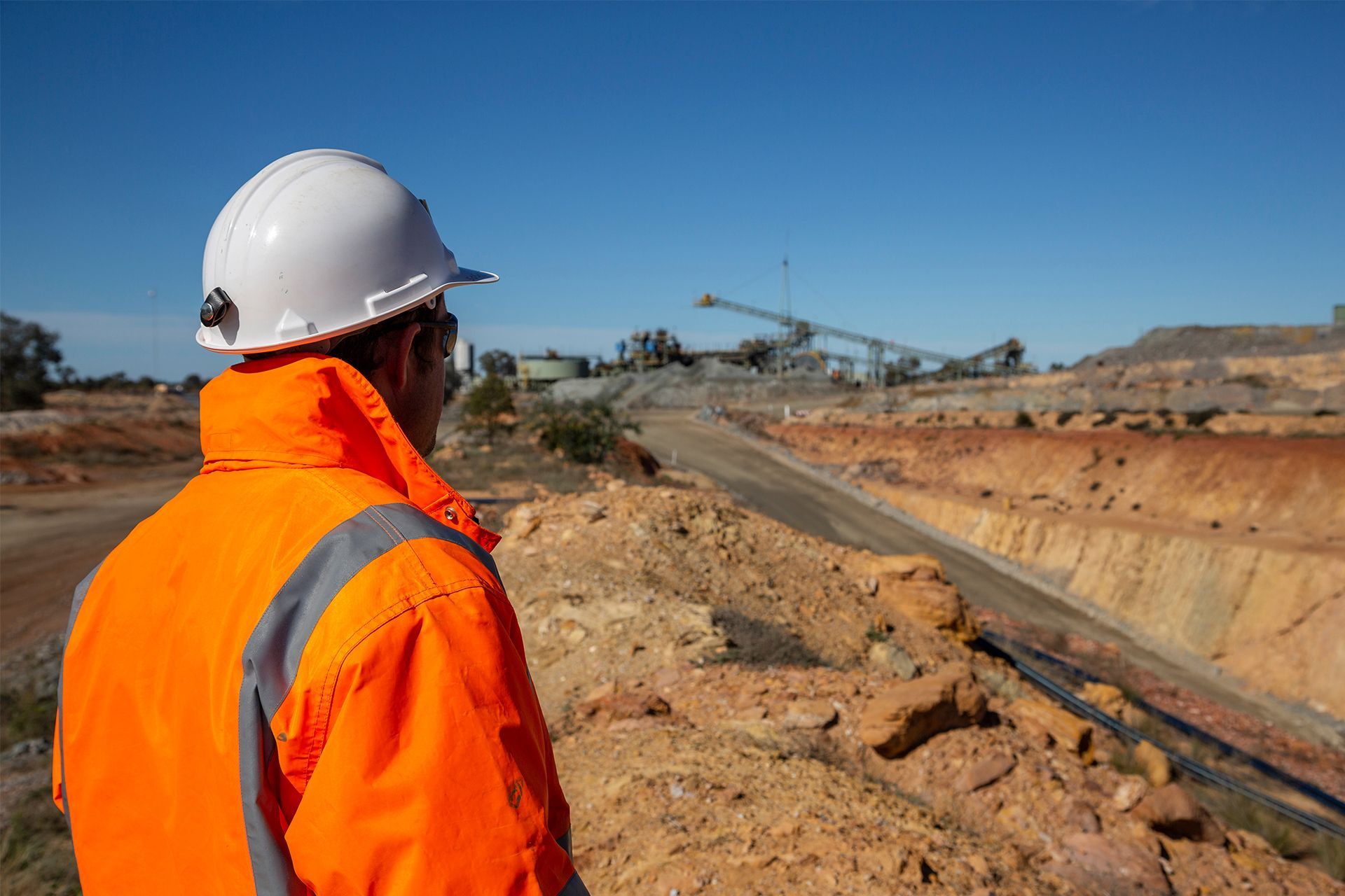 Worker in orange safety gear and white hard hat overlooking a mine site