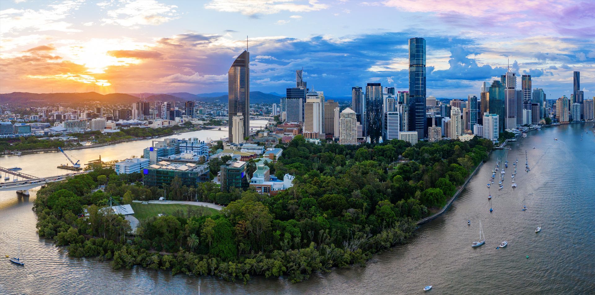 Sunset aerial of a Brisbane city skyline beside Brisbane river and green park waterfront
