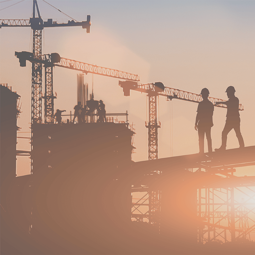 Construction site at sunset with silhouettes of workers and cranes.