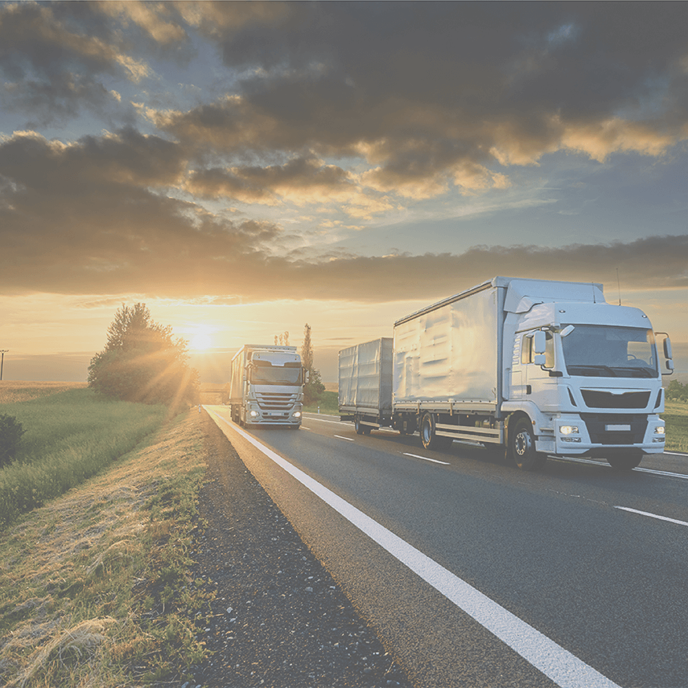 Two semi-trucks driving on a highway with a sunset in the background.