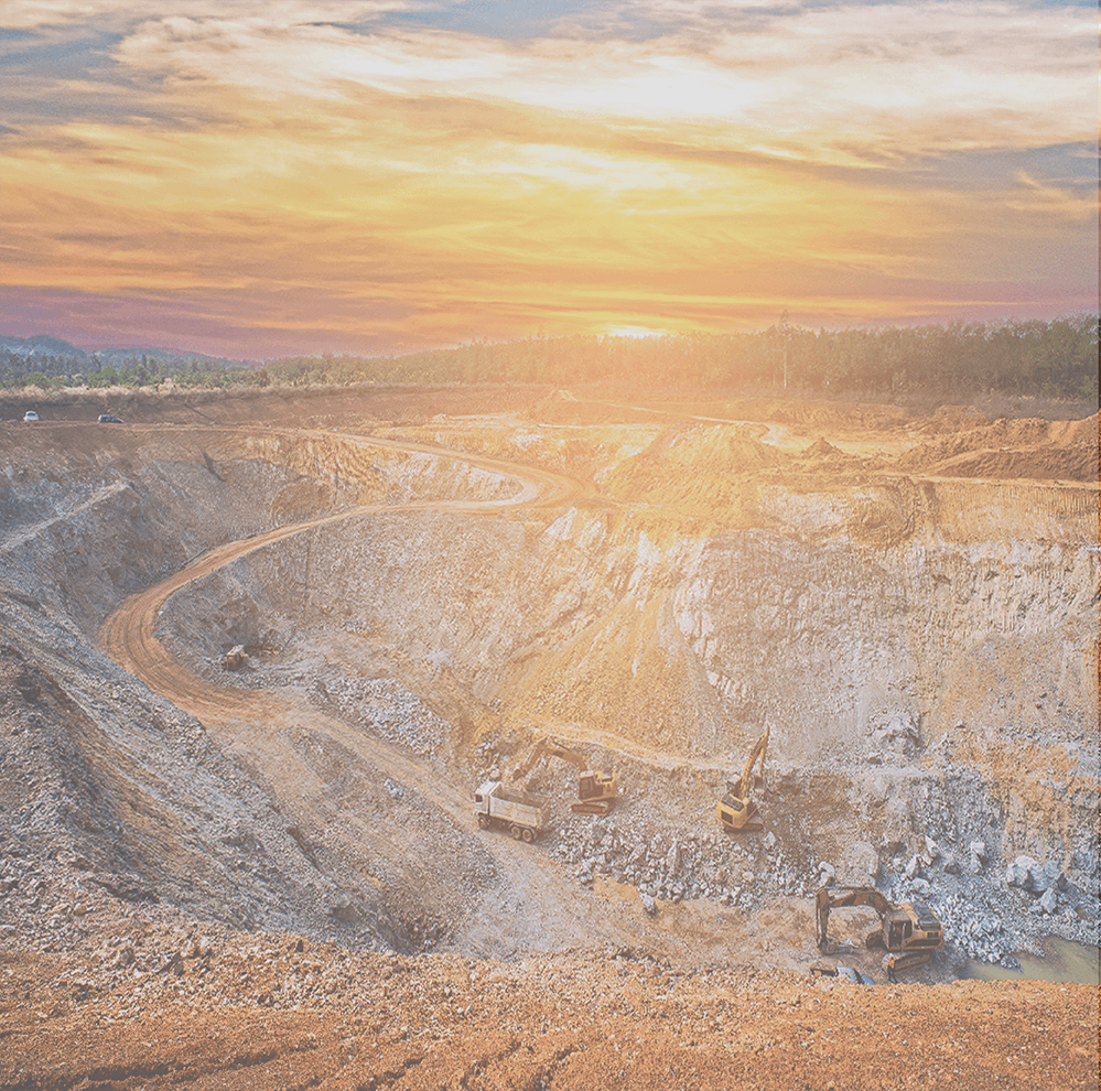 Open-pit mine at sunset with heavy machinery; warm orange sky, rocky terrain.