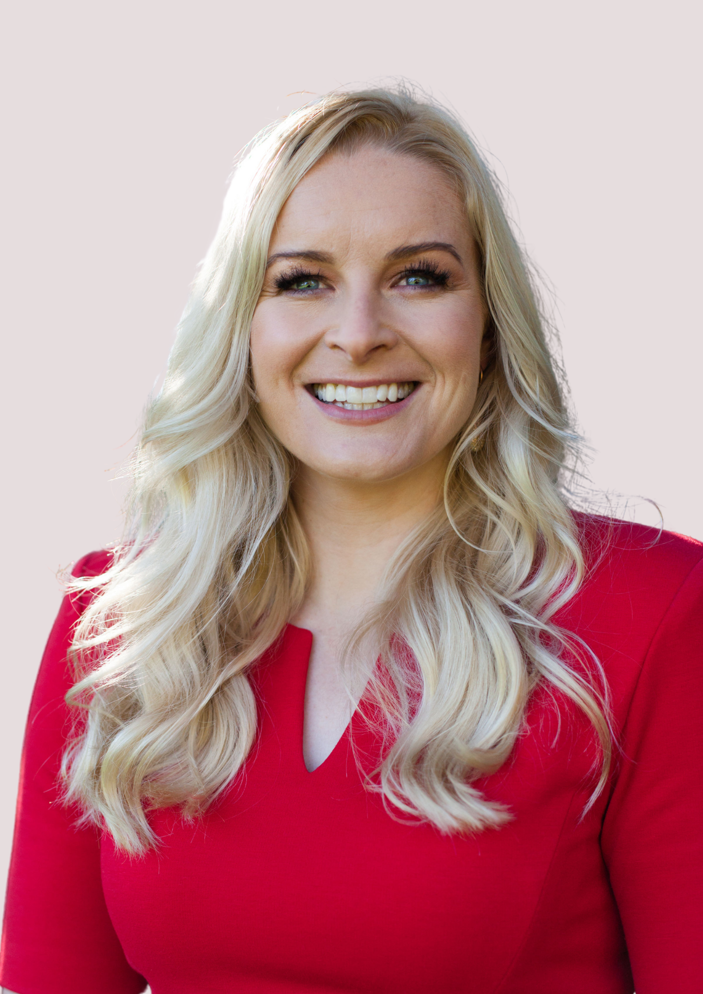 Blonde woman in red dress smiles at camera; outdoor setting with a light pink background.