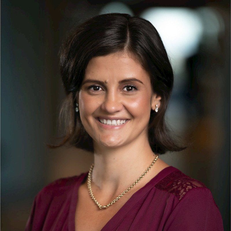 Woman with dark hair smiles, wearing a burgundy shirt and gold necklace.