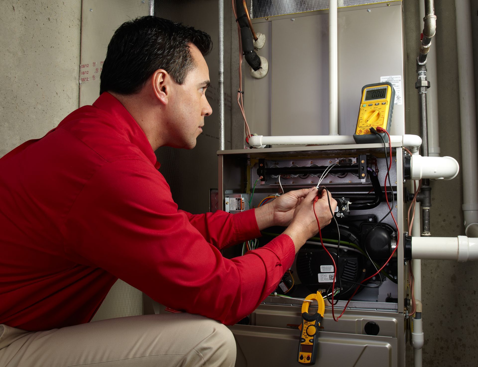 Man in red shirt examining furnace with a multimeter.