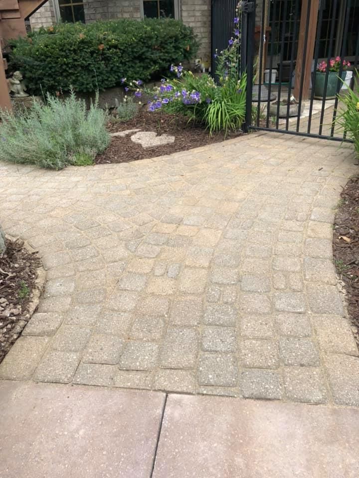 Curved stone paver walkway leading to a black gate beside garden shrubs and purple flowers.