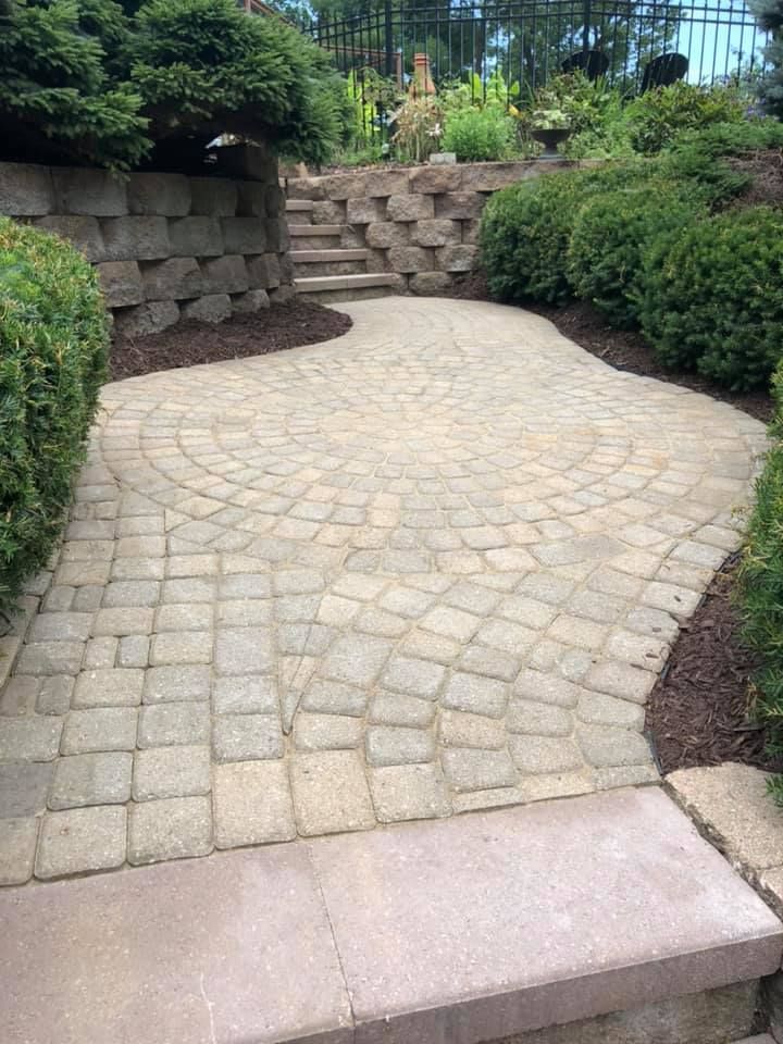 Curved stone paver walkway bordered by shrubs and a low stone retaining wall in a landscaped garden