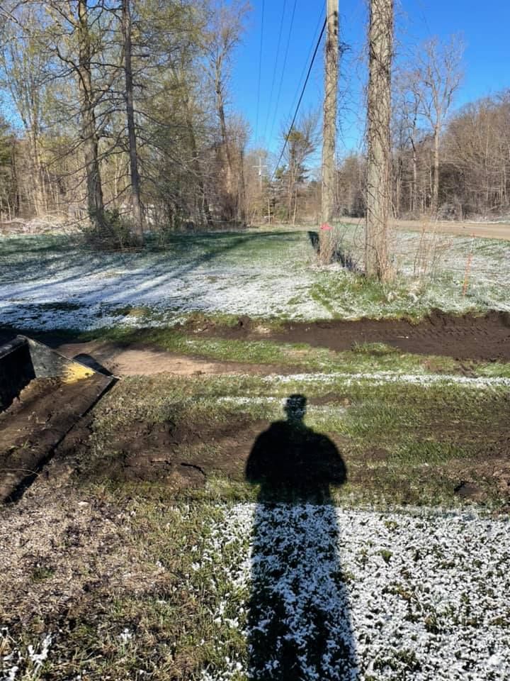 Snow-dusted dirt path in a wooded area with utility poles and a person's shadow in the foreground