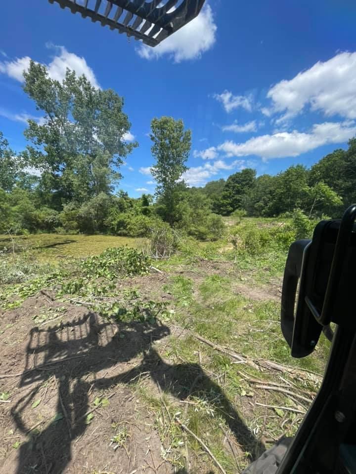 Lifting view from a tractor over a grassy field with trees and a bright blue sky with clouds