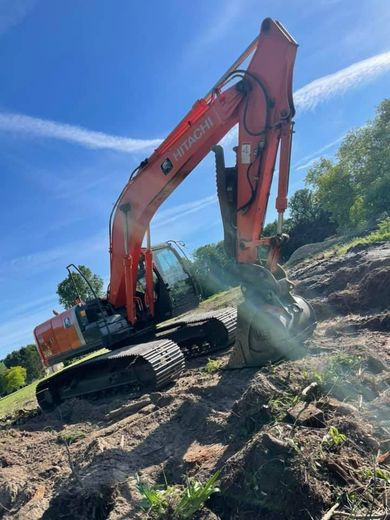 Orange excavator digging a trench on a sunny dirt slope under a blue sky