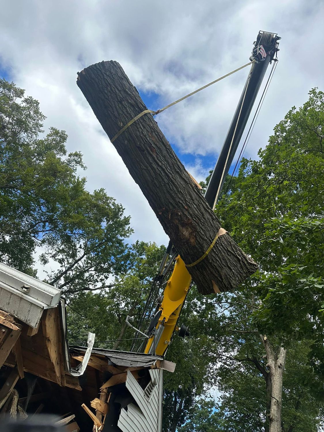 Broken utility pole being lifted by a crane near a house under a cloudy sky