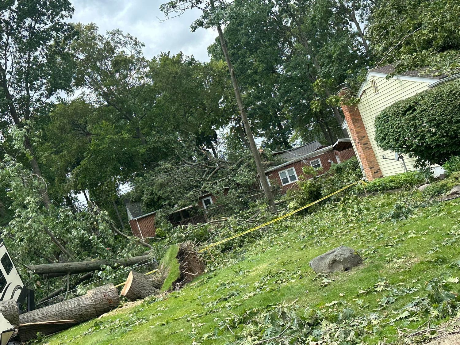 Storm-damaged yard with uprooted trees, broken branches, and scattered debris near a house