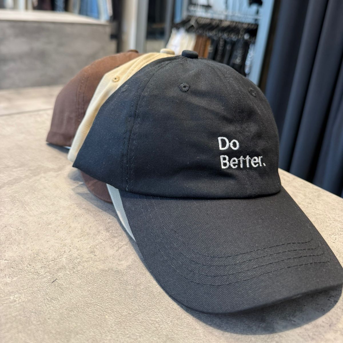 Tres gorras de béisbol apiladas: marrón, canela y negra. La gorra negra tiene bordado 