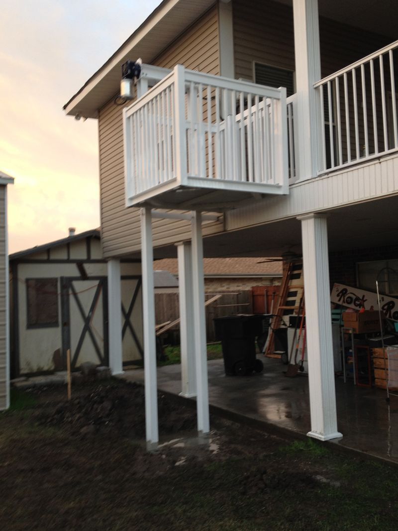 Elevated white house porch on stilts with stairs and balcony beside a garage at dusk Elevated white house porch on stilts with stairs and balcony beside a garage at dusk