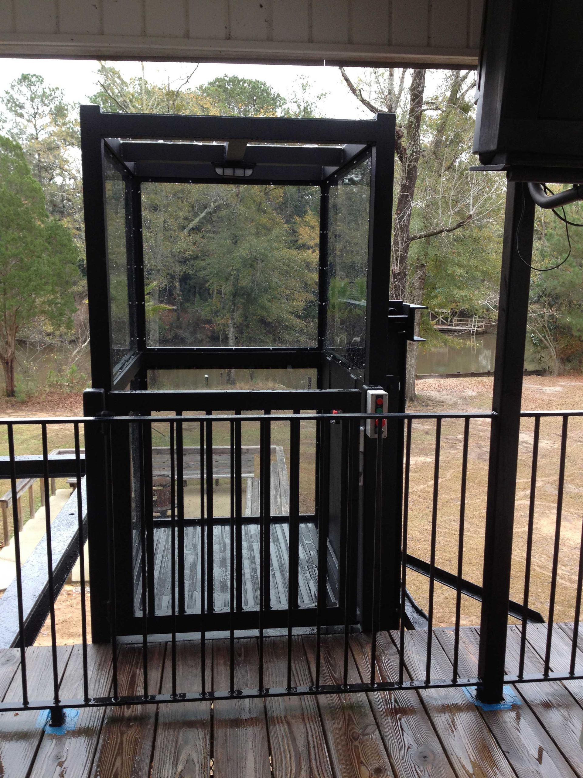 Black metal cage lift/elevator at an outdoor platform, viewed through a railing. Black metal cage lift/elevator at an outdoor platform, viewed through a railing.