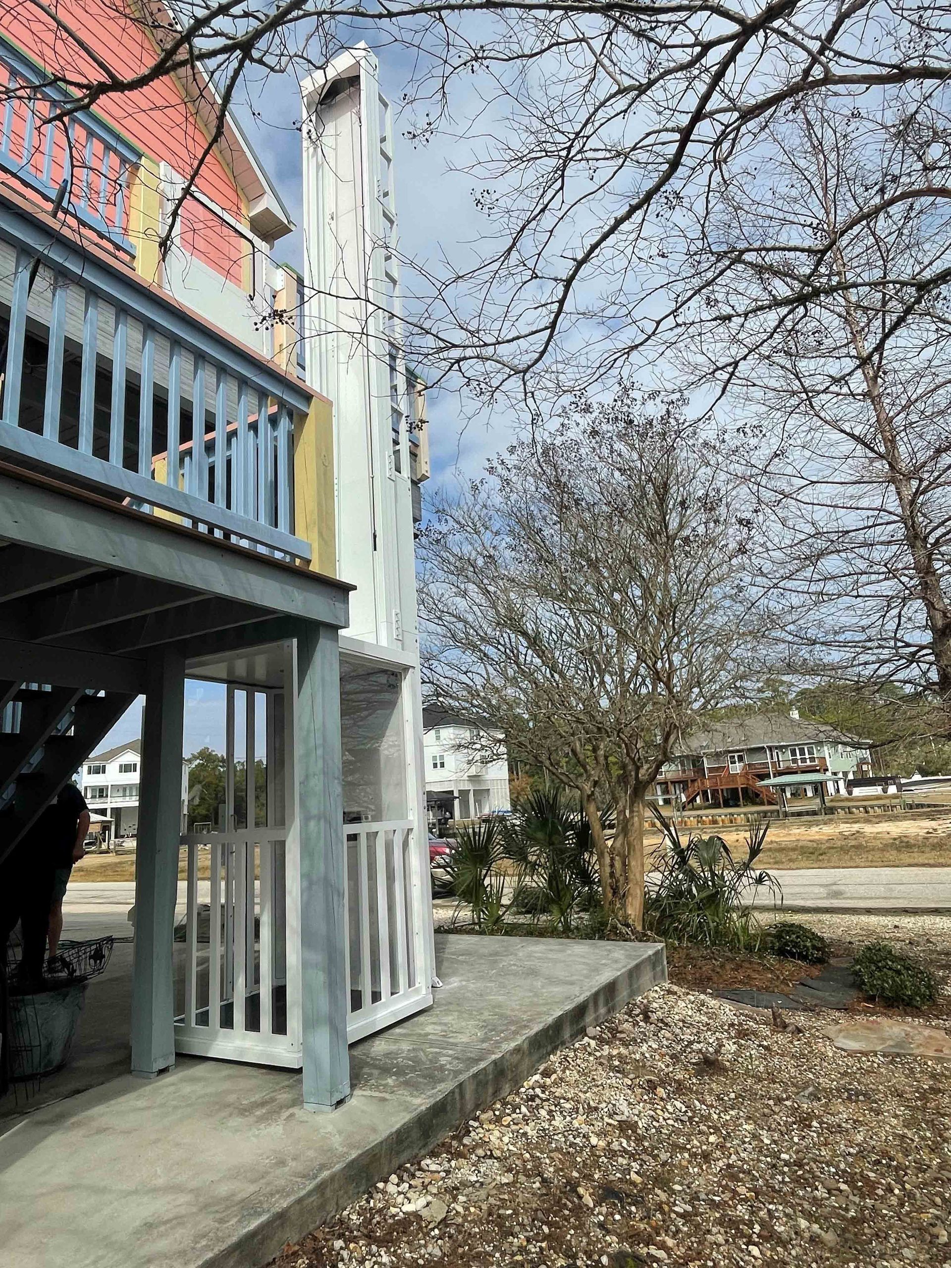Two-story house with blue balcony, white stairs, and leaf-covered yard under bare tree branches.