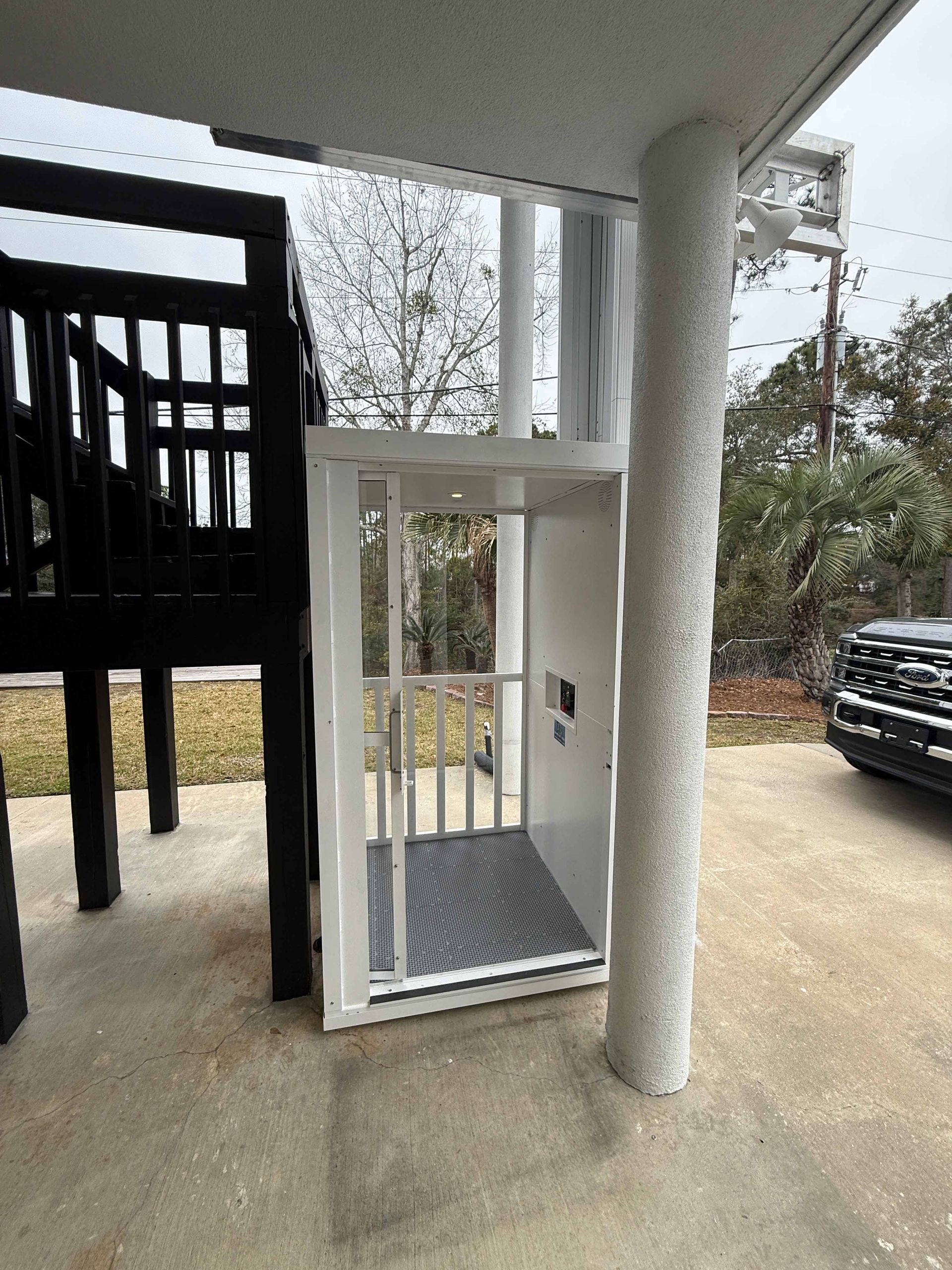 Outdoor wheelchair lift beside a porch, with a textured platform and white railings under a covered area