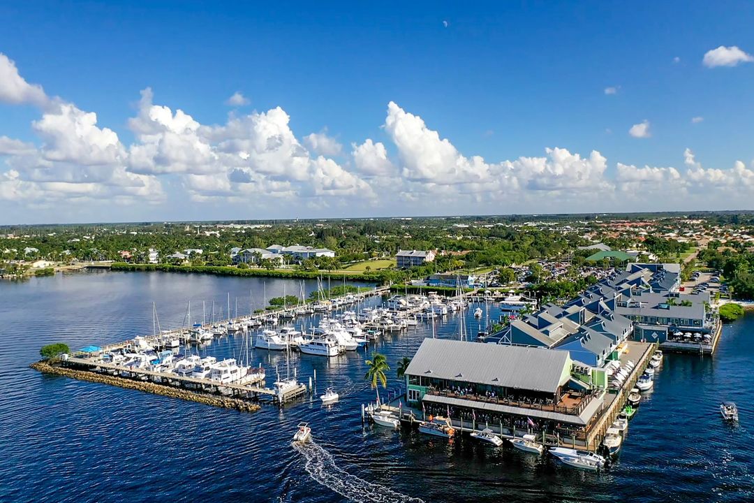 Boats docked at a marina with green buildings on water, under a blue sky with clouds.