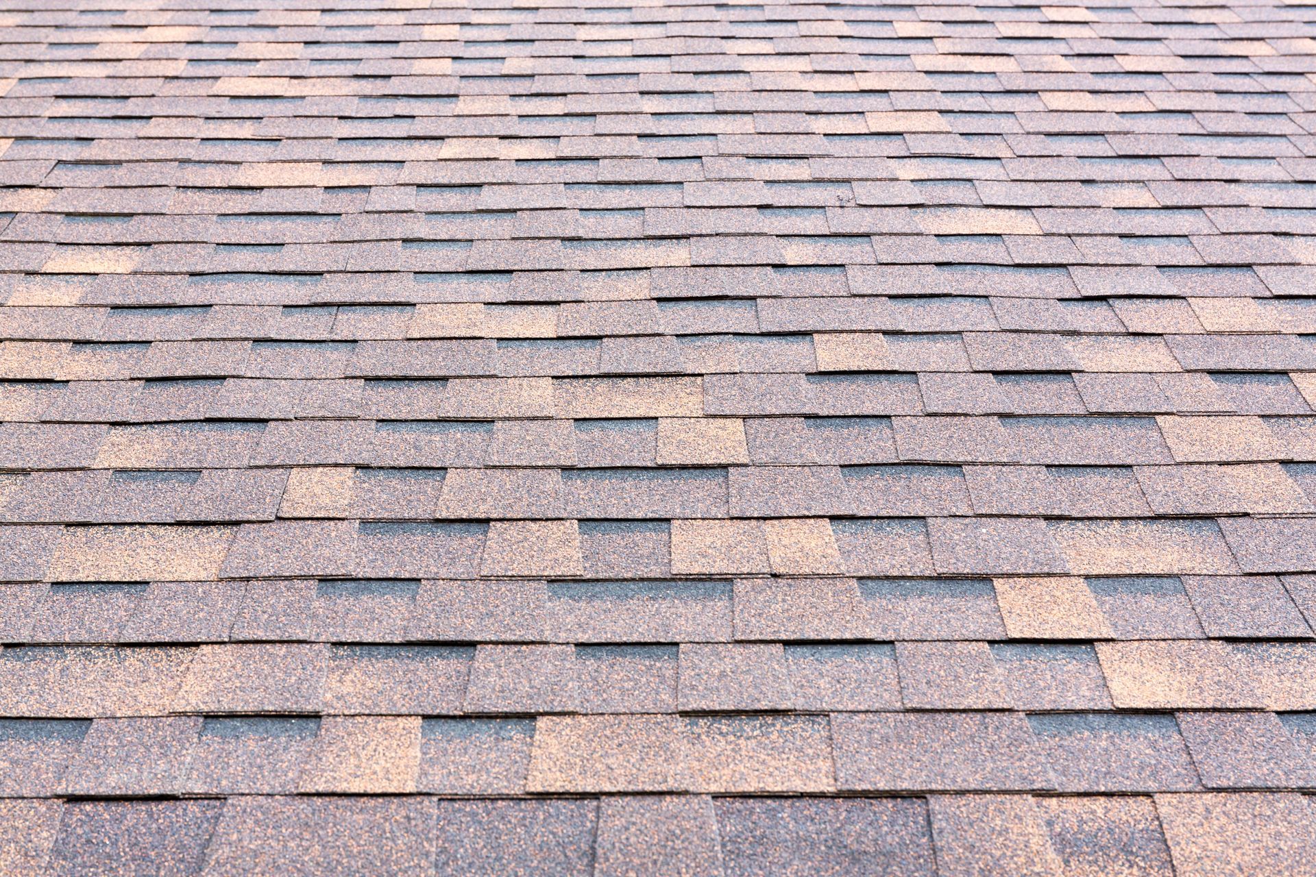 Worker nailing gray roof shingles on a roof under construction