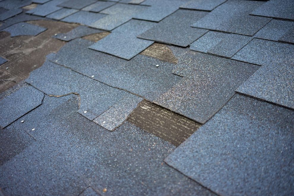 Roofing worker installing dark shingles on a house roof beside a brick chimney