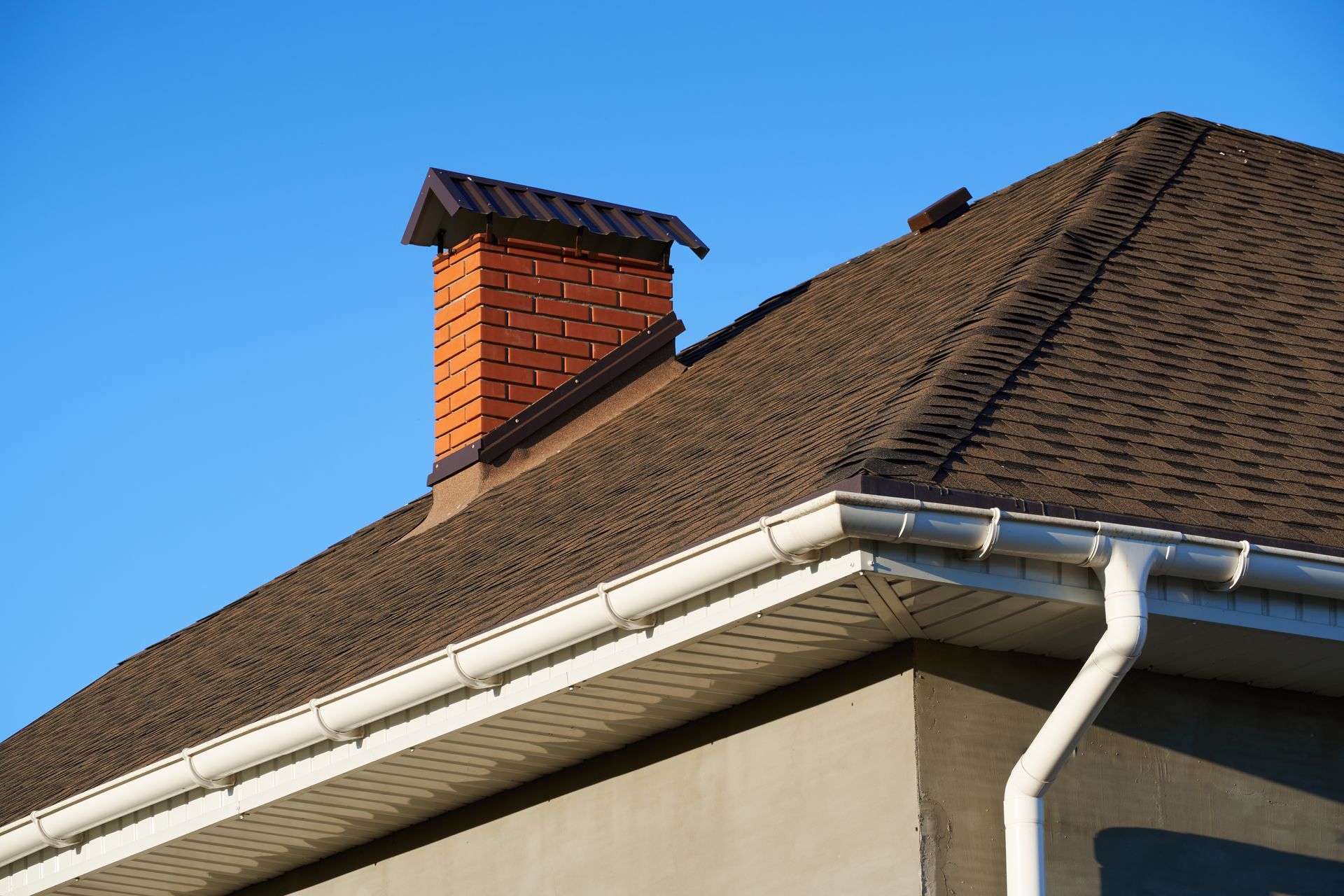 House roof with white gutter and red brick chimney against a blue sky