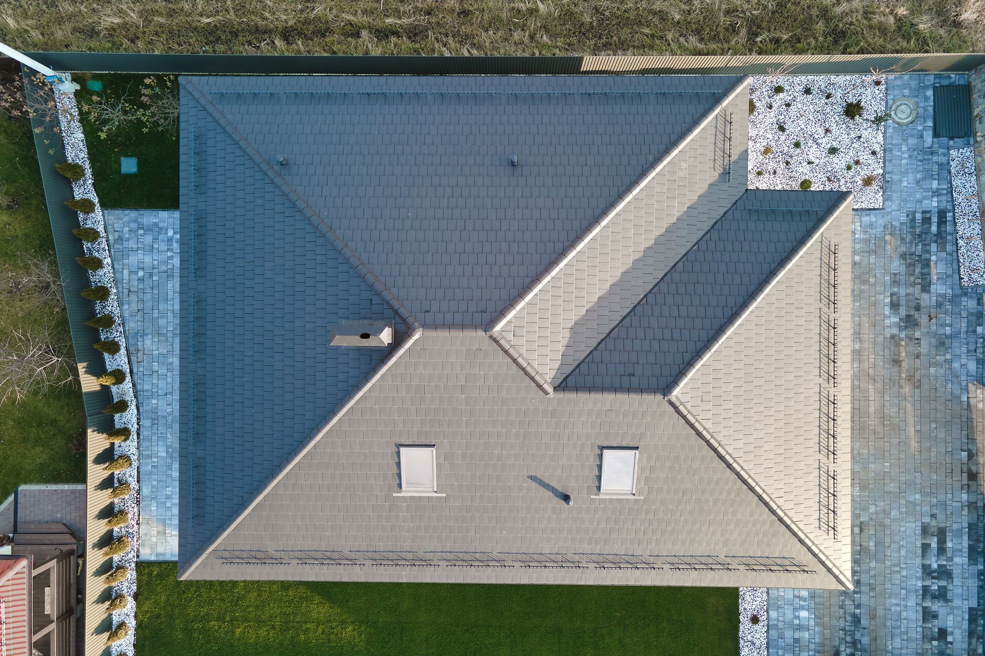 Aerial view of a gray-roofed house with a central chimney and surrounding yard.