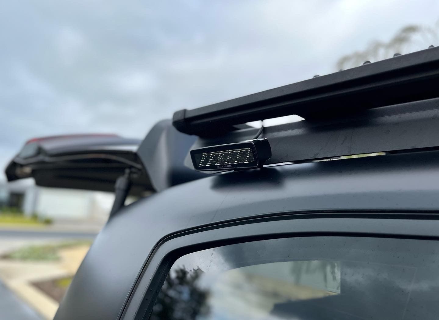Compact rear work light installed on roof rack providing campsite illumination for touring vehicles.