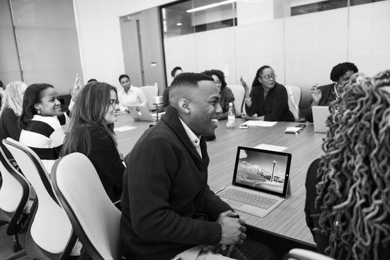 A group of people are sitting around a conference table with laptops.