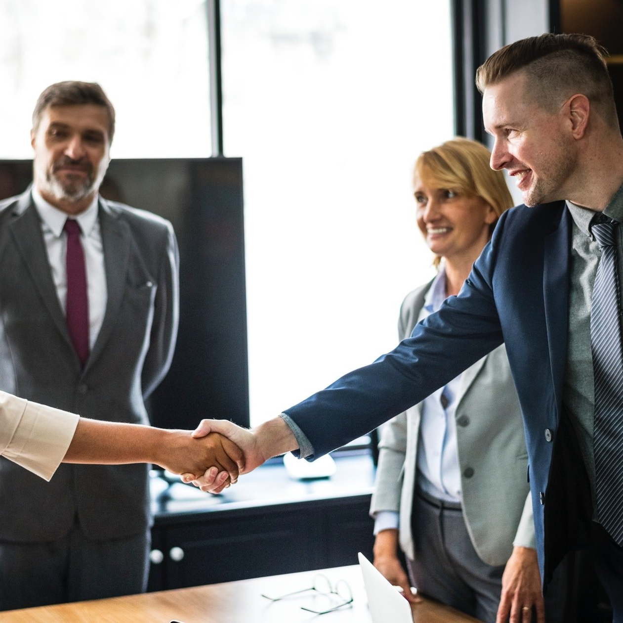A man in a suit shakes hands with a woman in a white shirt