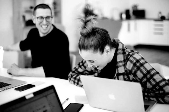 A man and a woman are sitting at a table with laptops.