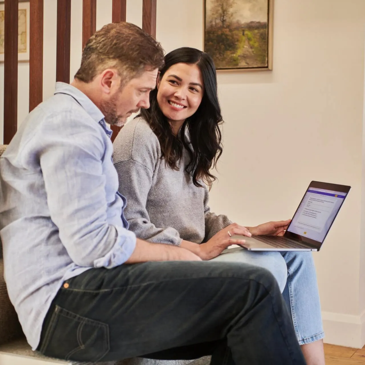 A man and a woman are sitting on a couch looking at a laptop.