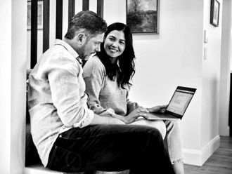 A man and a woman are sitting on a couch looking at a laptop.