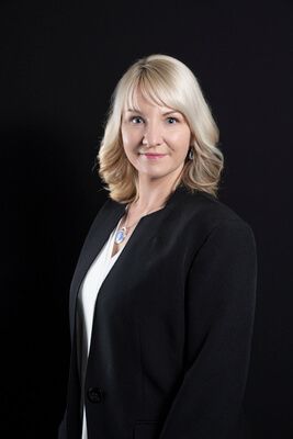 Professional portrait of a woman in a black blazer against a dark background
