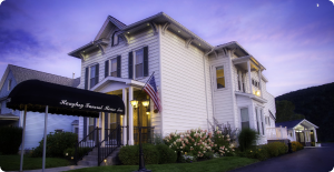 White historic house with lit windows and a black awning at dusk