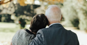 Two people sitting close together outdoors, one resting their head on the other's shoulder.