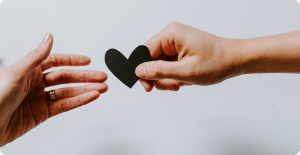 Two hands reaching toward a black heart shape on a light background