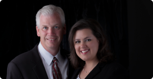 Two people in business attire smiling against a dark background
