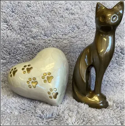 Cream heart-shaped ornament with paw prints beside a glossy dark cat figurine on a gray plush background