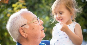 Older man smiles at a young child outdoors, looking up at her as she smiles back.