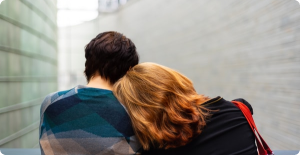 Two people leaning together on a moving walkway in a bright tunnel, seen from behind