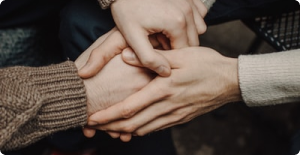 Two hands clasped in a supportive handshake, with others gently stacked on top.