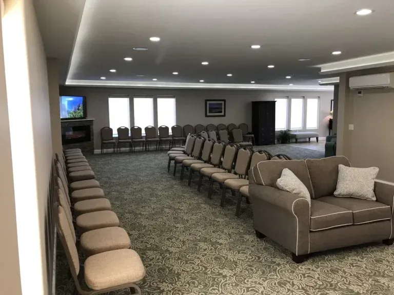 Empty waiting room with rows of beige chairs, a gray loveseat, and TV screens on the wall.