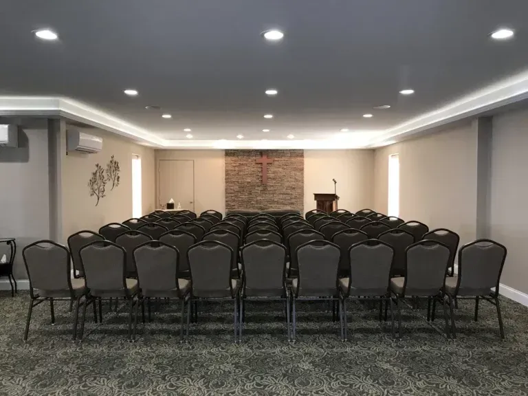 Empty conference room with rows of black chairs facing a podium and brick accent wall